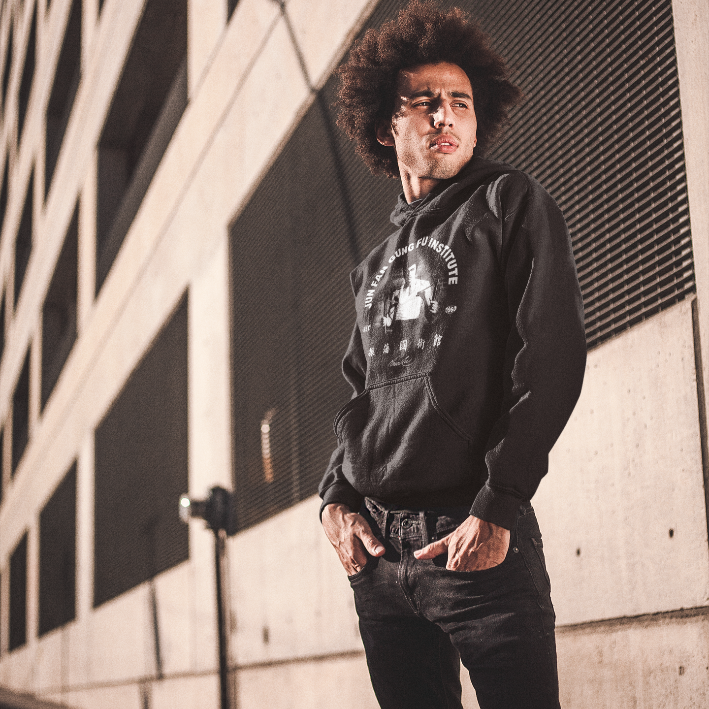 Man with curly hair in a black Bruce Lee JFGFI hoodie and jeans